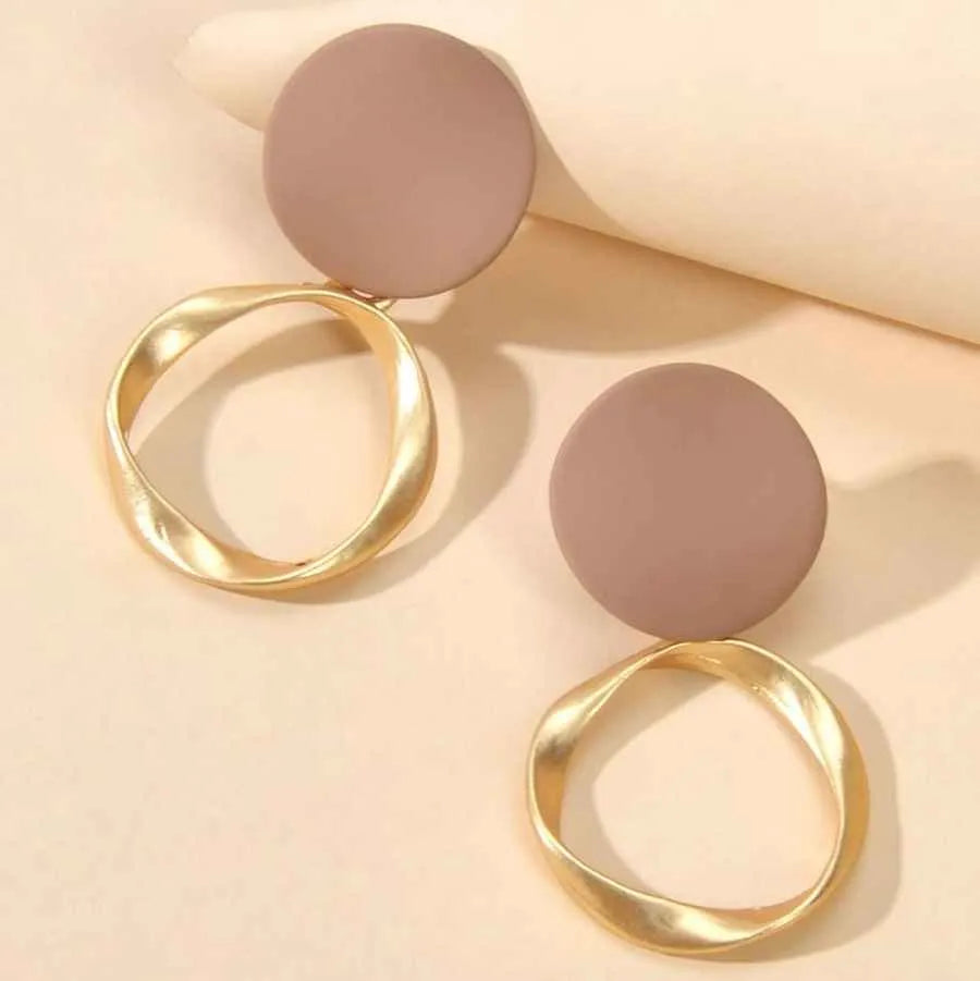Gold and beige earrings on a light pink background